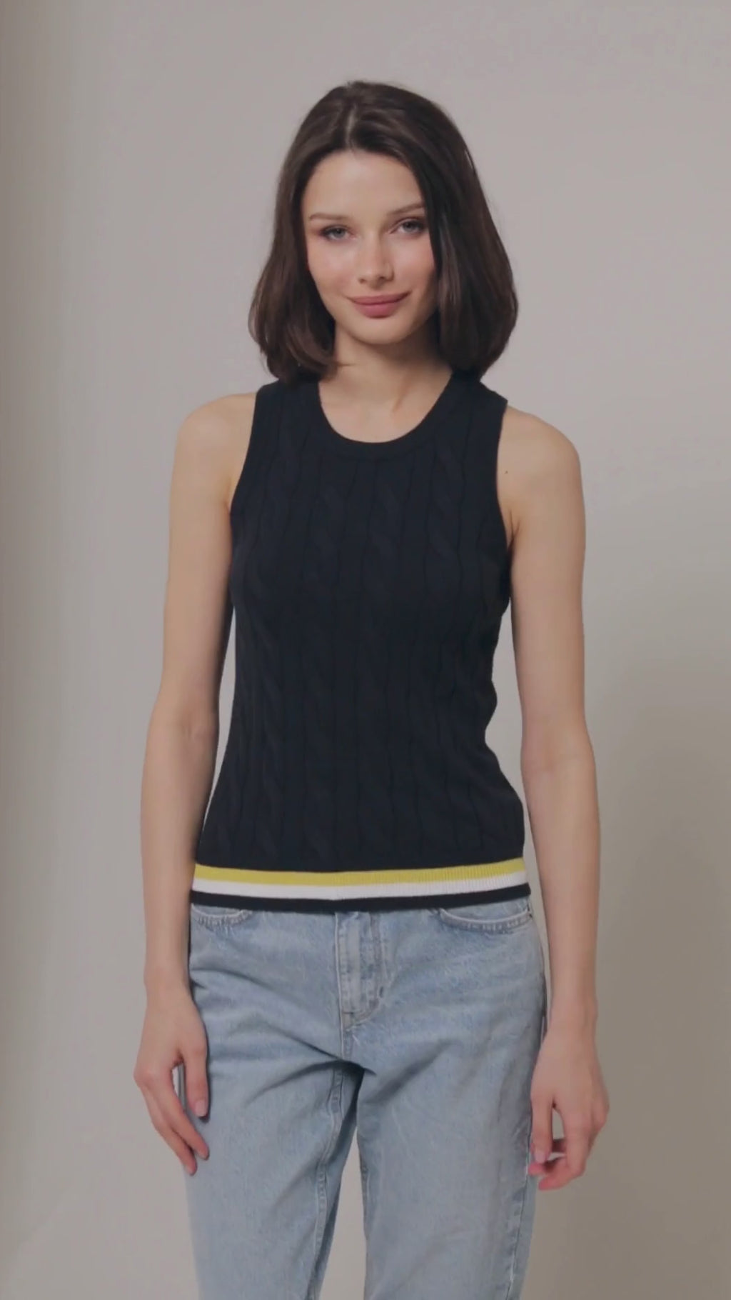 Video of model turning 360 degrees wearing navy cable knit sweater tank top with yellow, white and navy stripe detail on bottom hem